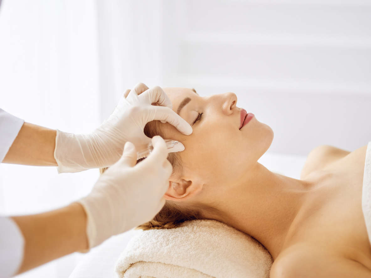 Beautiful woman receiving beauty injections with closed eyes. Beautician doctor hands doing beauty procedure to female face with syringe. Cosmetic medicine and surgery concept HALO AESTHETICS BAR - West Hollywood’s Best-Kept Beauty Secret
